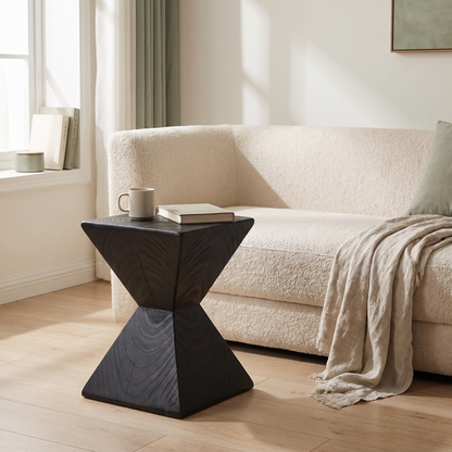 Kaya hourglass side table in black wood beside a cream boucle sofa in a bright living room