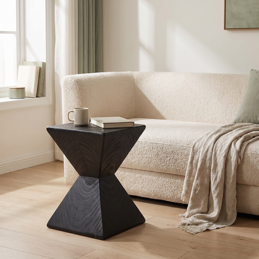 Kaya hourglass side table in black wood beside a cream boucle sofa in a bright living room