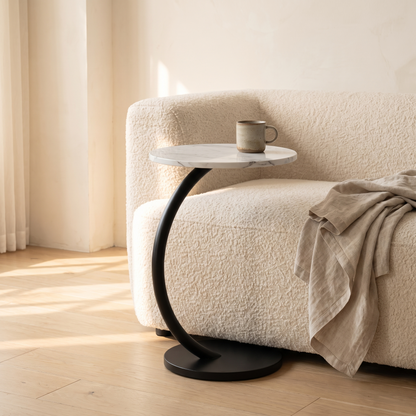 Orla Curve Side Table in white marble effect with black frame beside a cream boucle sofa